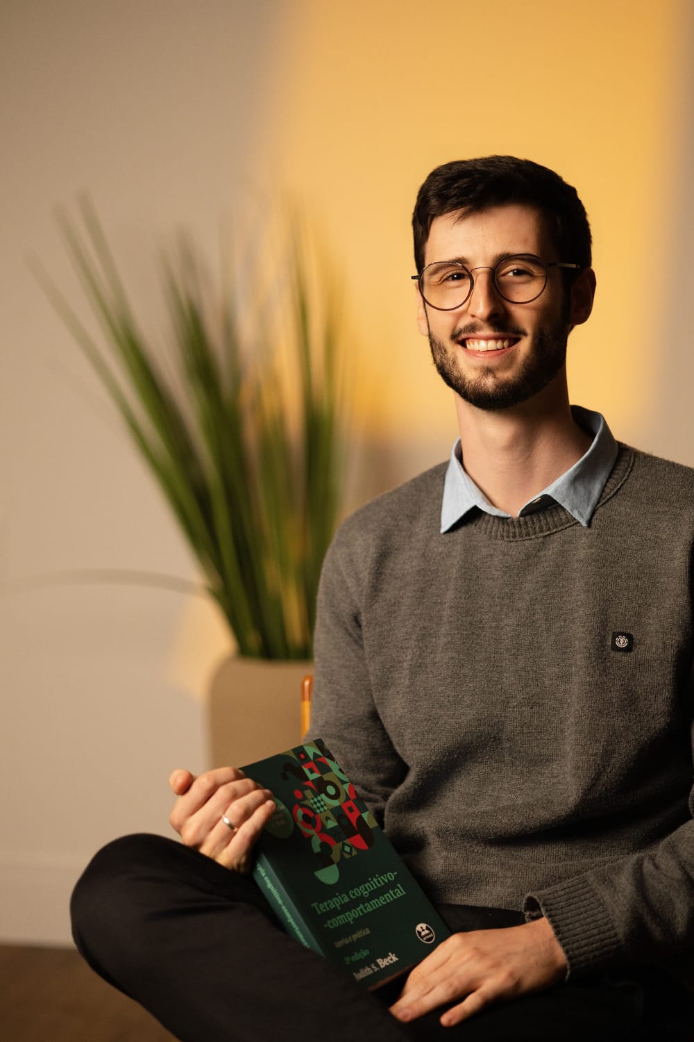 Tiago Kraisch sorrindo com um livro de terapia cognitivo-comportamental